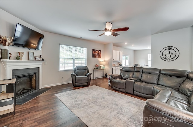 living area featuring dark wood-type flooring, a fireplace, baseboards, and a ceiling fan