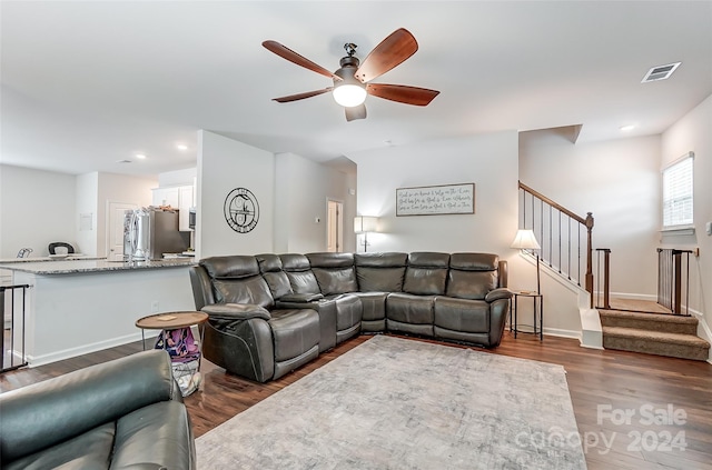 living room with dark wood-style flooring, visible vents, ceiling fan, baseboards, and stairs