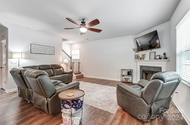 living area with stairs, dark wood-type flooring, a fireplace, and a ceiling fan