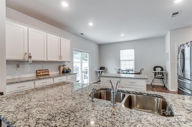 kitchen with light stone counters, freestanding refrigerator, white cabinetry, and visible vents