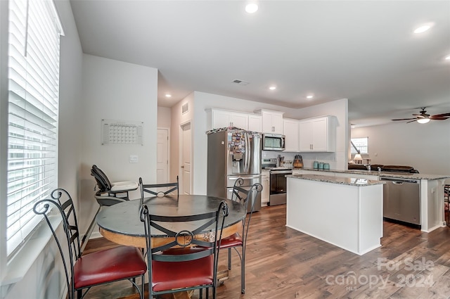 kitchen with light stone countertops, stainless steel appliances, visible vents, white cabinetry, and a center island