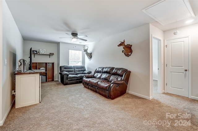 living area with attic access, light colored carpet, baseboards, and a ceiling fan