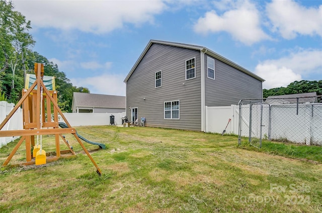 rear view of house with a yard, a playground, and fence