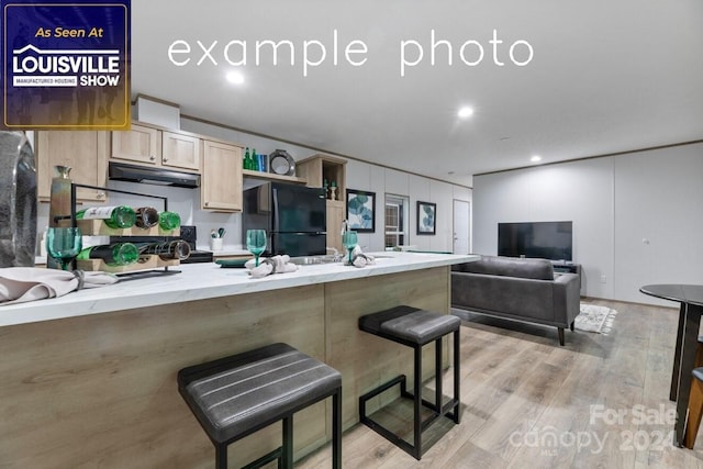 kitchen with a breakfast bar, light brown cabinetry, light hardwood / wood-style flooring, and black refrigerator