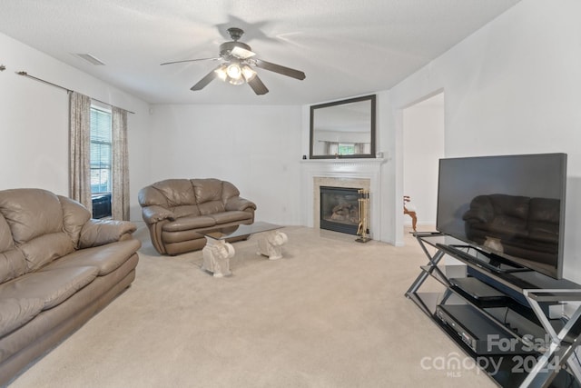 living room with a tiled fireplace, light colored carpet, ceiling fan, and a textured ceiling