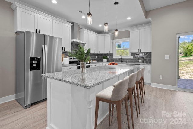 kitchen featuring a wealth of natural light, stainless steel appliances, wall chimney exhaust hood, and a center island