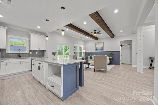 kitchen with light stone counters, a center island, white cabinets, a barn door, and ceiling fan