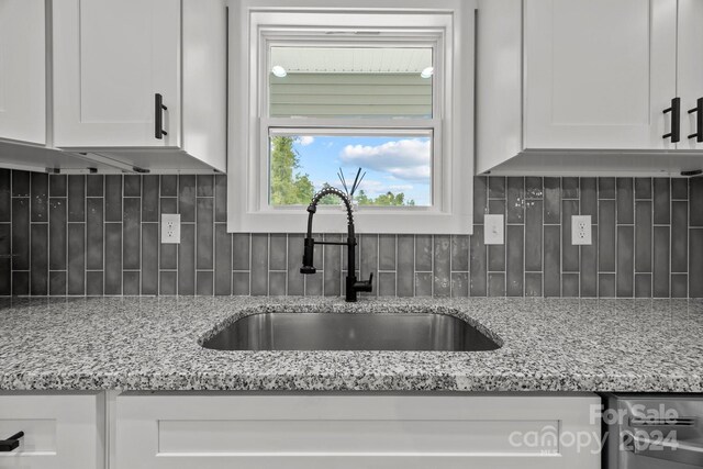 kitchen featuring tasteful backsplash, sink, light stone counters, and white cabinets