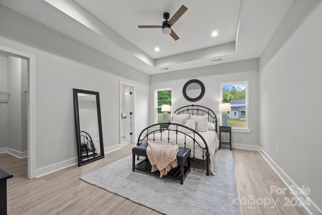 bedroom with light hardwood / wood-style flooring, ensuite bath, ceiling fan, and a raised ceiling