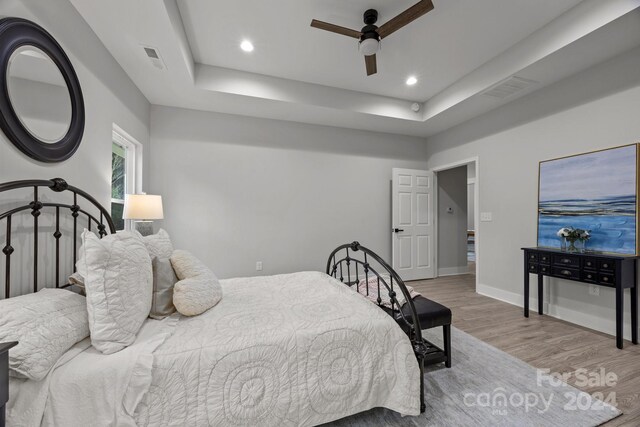 bedroom featuring ceiling fan, a raised ceiling, and light hardwood / wood-style floors