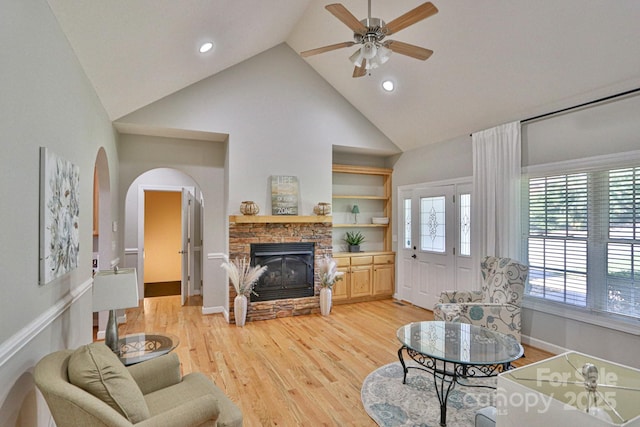 living room with ceiling fan, a fireplace, high vaulted ceiling, and light wood-type flooring