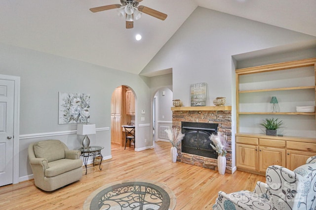 living room with a stone fireplace, ceiling fan, high vaulted ceiling, and light wood-type flooring