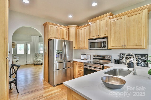 kitchen with appliances with stainless steel finishes, light hardwood / wood-style flooring, light brown cabinetry, and sink