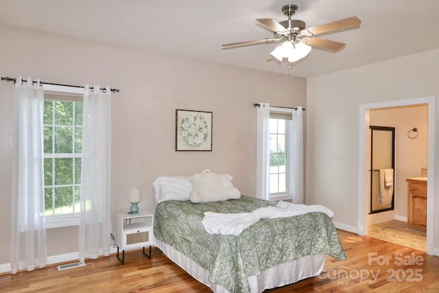 bedroom with multiple windows, ensuite bathroom, ceiling fan, and hardwood / wood-style flooring