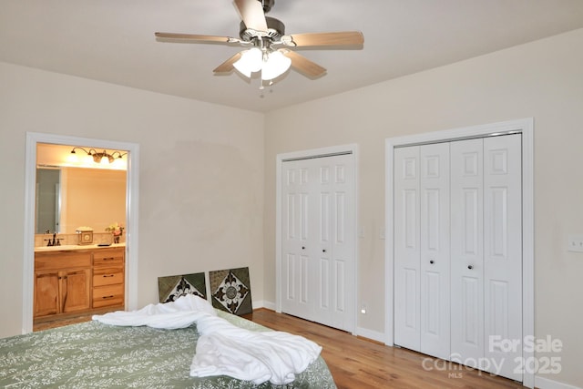 bedroom with two closets, sink, ceiling fan, connected bathroom, and wood-type flooring