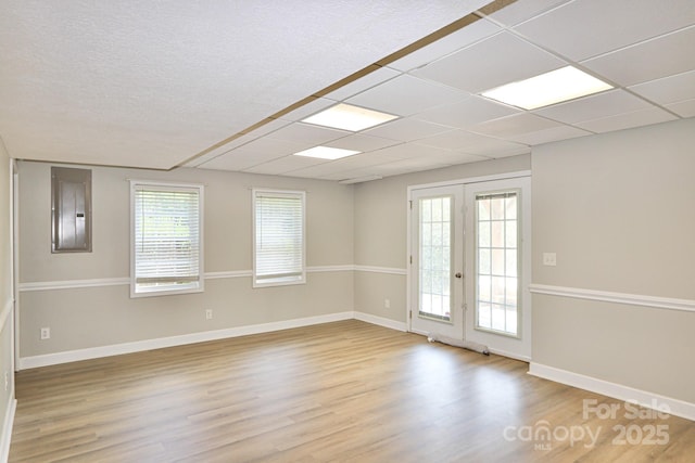 unfurnished room with a drop ceiling, wood-type flooring, electric panel, and french doors