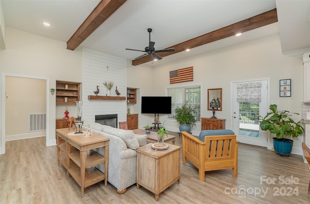 living room featuring a large fireplace, ceiling fan, beamed ceiling, and light hardwood / wood-style floors