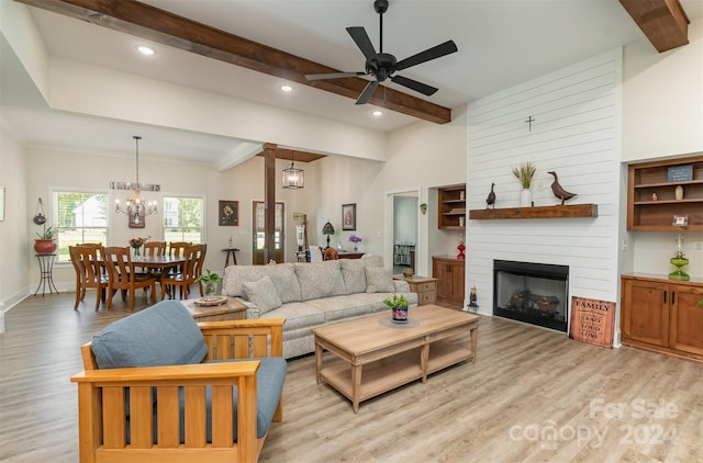 living room featuring ceiling fan with notable chandelier, beamed ceiling, light hardwood / wood-style flooring, and a large fireplace