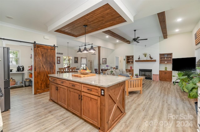 kitchen with light wood-type flooring, beamed ceiling, a large fireplace, ceiling fan, and a barn door