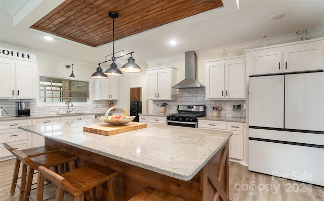 kitchen featuring stainless steel range with gas stovetop, white fridge, backsplash, light wood-type flooring, and wall chimney range hood