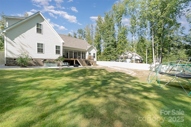 rear view of property with stairs, a trampoline, fence, and a lawn