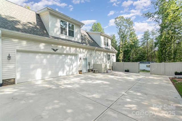 view of property exterior with a garage, a shingled roof, fence, and concrete driveway