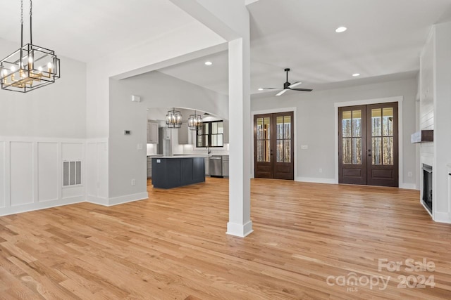 unfurnished living room featuring ceiling fan with notable chandelier, light hardwood / wood-style flooring, and french doors