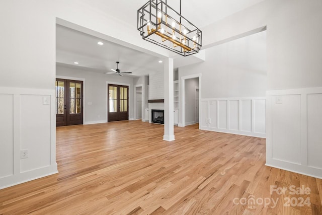 unfurnished living room featuring a fireplace, light hardwood / wood-style flooring, ceiling fan with notable chandelier, and french doors