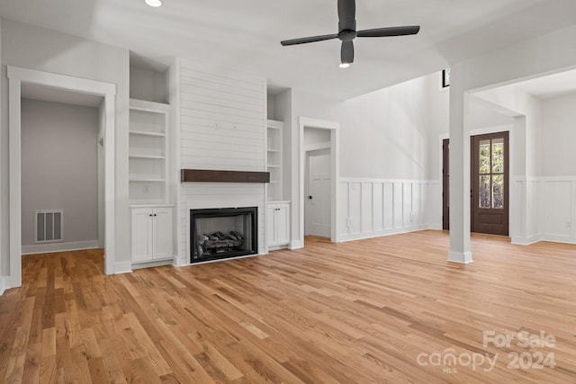 unfurnished living room featuring light wood-type flooring, a large fireplace, ceiling fan, and built in shelves