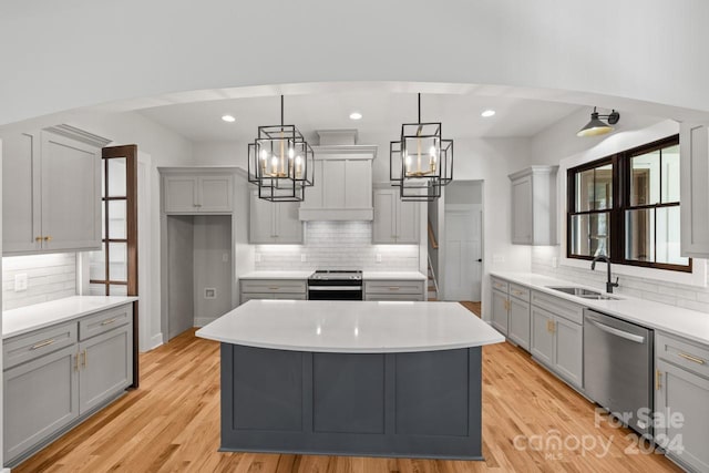 kitchen featuring light wood-type flooring, appliances with stainless steel finishes, decorative backsplash, a kitchen island, and gray cabinetry