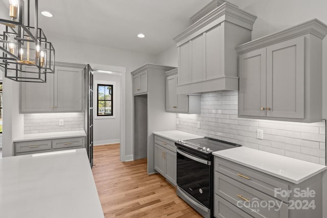 kitchen with light wood-type flooring, decorative backsplash, stainless steel range with electric cooktop, gray cabinets, and hanging light fixtures