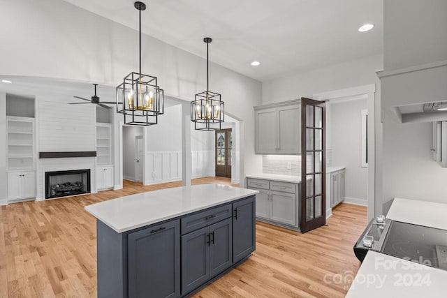 kitchen with light hardwood / wood-style floors, decorative backsplash, a large fireplace, gray cabinetry, and ceiling fan with notable chandelier