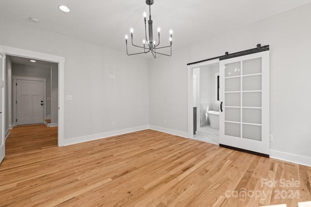 unfurnished dining area featuring an inviting chandelier, light wood-type flooring, and a barn door