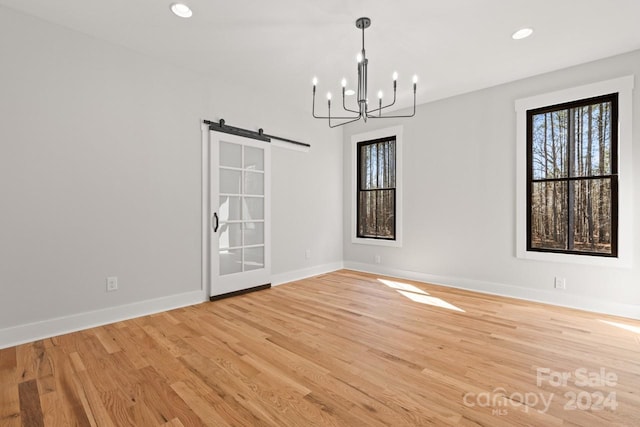 unfurnished room featuring light wood-type flooring, an inviting chandelier, and a barn door