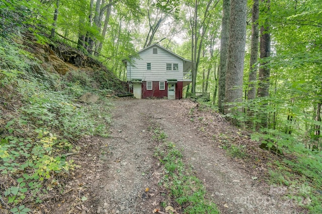 view of side of property featuring dirt driveway and a view of trees