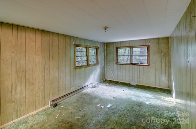 carpeted spare room featuring a baseboard heating unit and wood walls