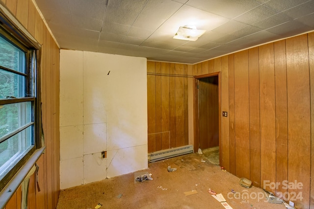 empty room featuring a baseboard radiator, a healthy amount of sunlight, and wood walls