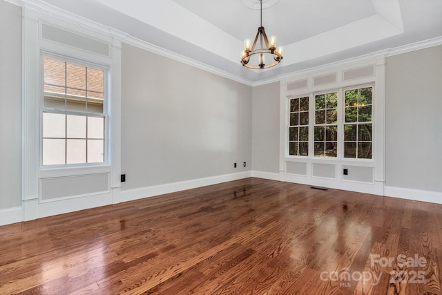 unfurnished dining area featuring hardwood / wood-style floors, ornamental molding, a raised ceiling, and a chandelier