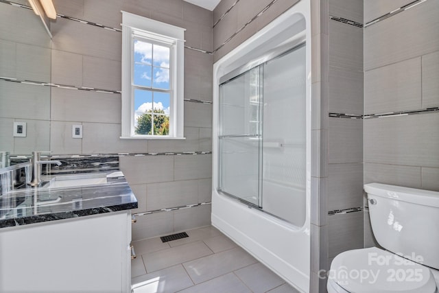 full bathroom with bath / shower combo with glass door, tile walls, vanity, toilet, and tile patterned floors