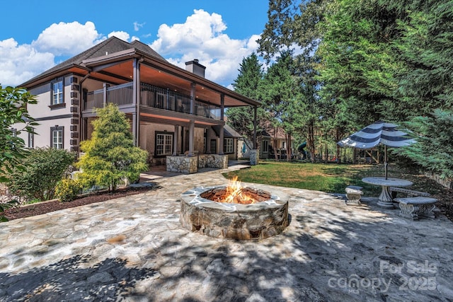 rear view of property featuring a balcony, an outdoor fire pit, a patio area, and a lawn