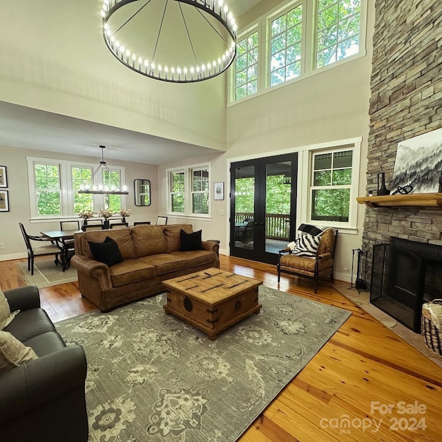 living room with a stone fireplace, french doors, an inviting chandelier, and light hardwood / wood-style flooring