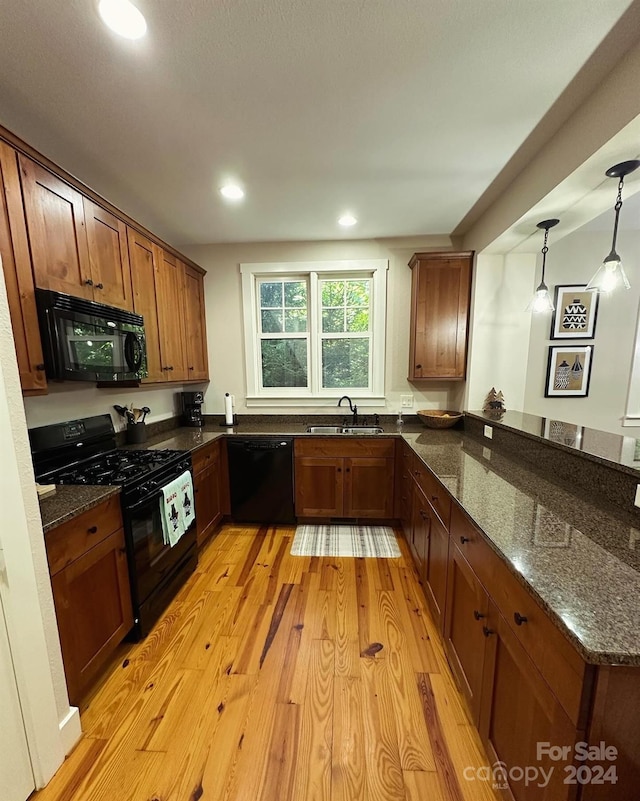 kitchen with dark stone counters, decorative light fixtures, black appliances, sink, and light hardwood / wood-style floors