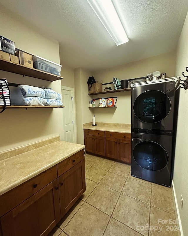 laundry area featuring a textured ceiling, cabinets, light tile patterned floors, and stacked washer / dryer