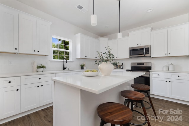 kitchen with hanging light fixtures, sink, a kitchen island, white cabinetry, and appliances with stainless steel finishes