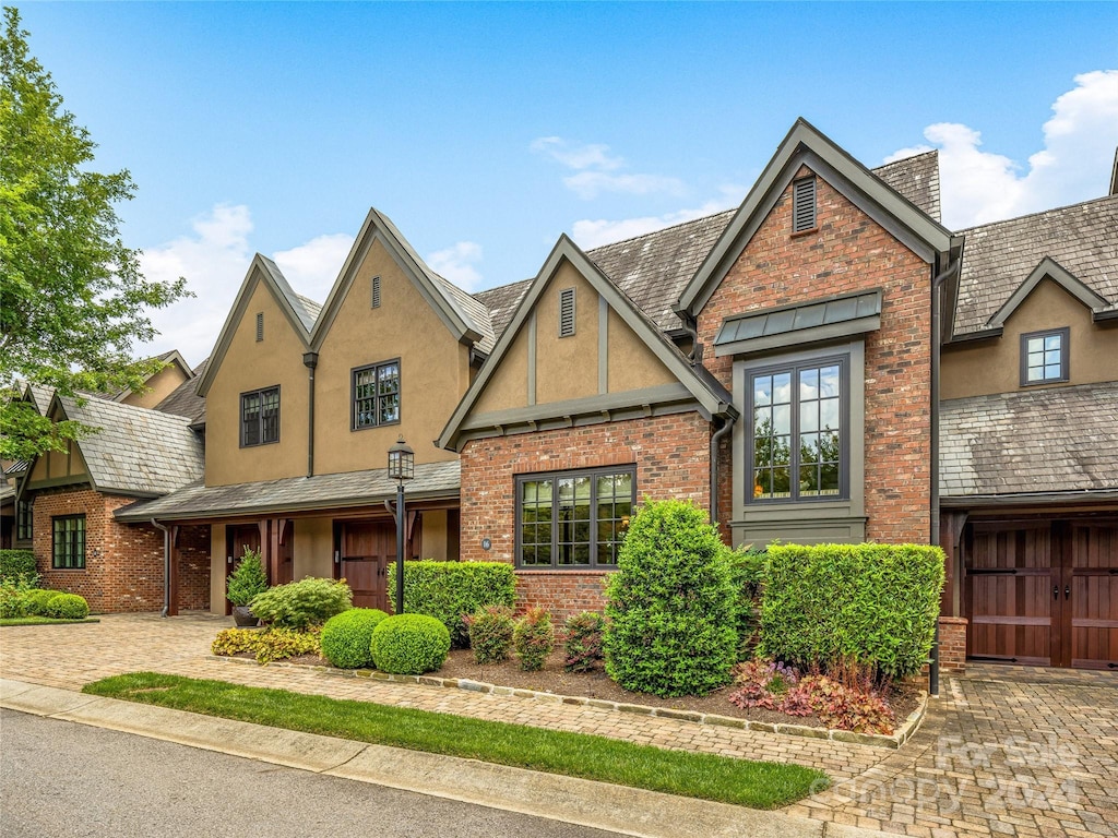 tudor house featuring a garage, stucco siding, decorative driveway, and brick siding