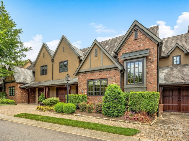 tudor house featuring a garage, stucco siding, decorative driveway, and brick siding