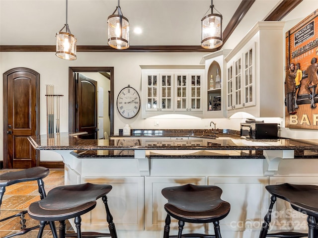 kitchen featuring dark stone counters, hanging light fixtures, a kitchen bar, light tile patterned floors, and crown molding