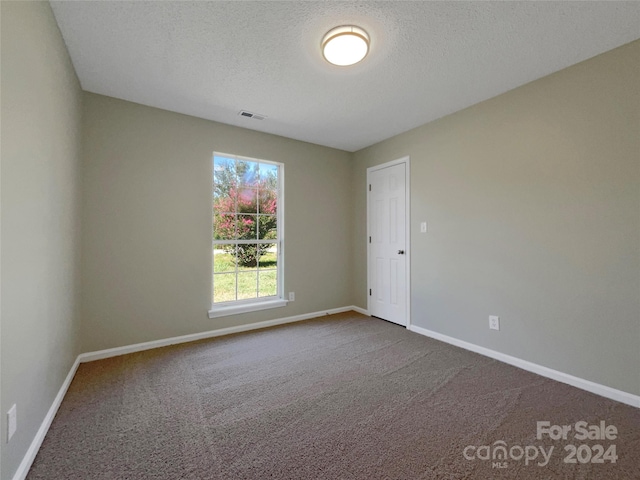 unfurnished room with a textured ceiling, carpet floors, visible vents, and baseboards