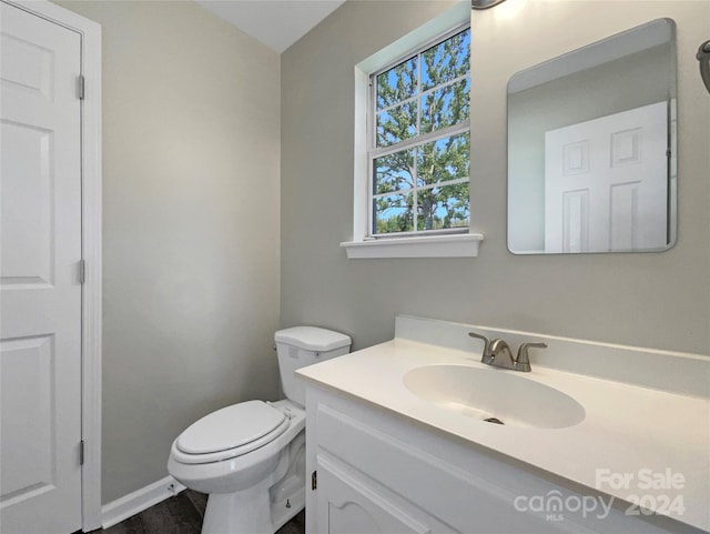 half bathroom with toilet, baseboards, and vanity