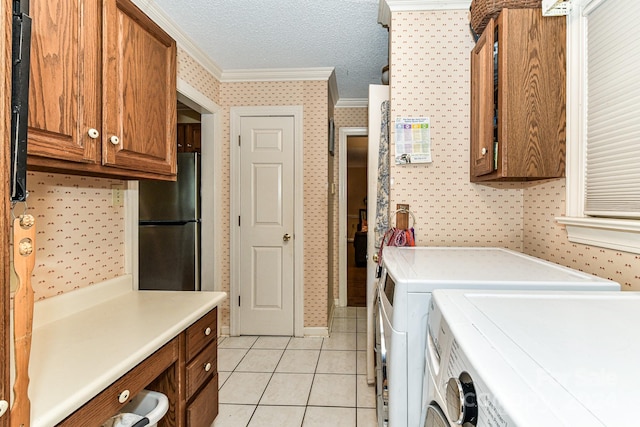 laundry area with cabinets, a textured ceiling, washing machine and clothes dryer, light tile patterned floors, and crown molding